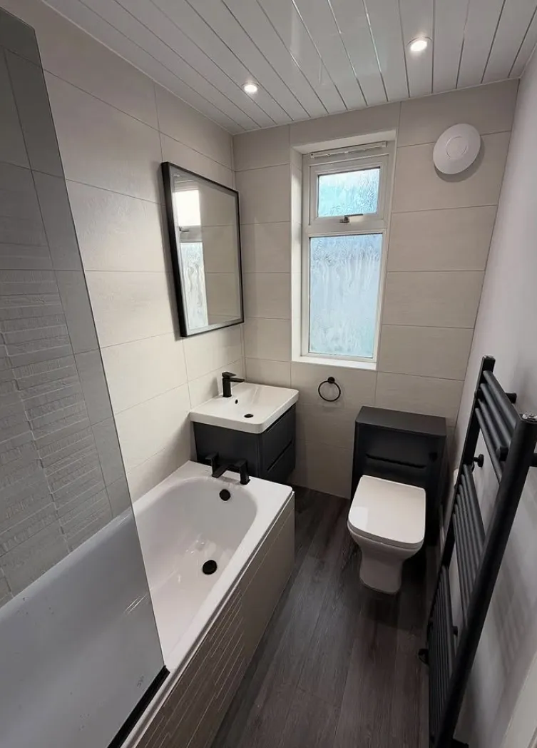 Bathroom in cream tiling with black brassware, a black vanity unit and a black towel radiator over a dark wood floor