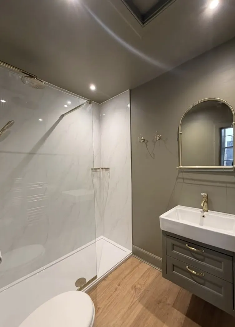 Shower room with sage green walls, marble-effect panelling, an arched brass mirror and a grey vanity unit on an oak floor