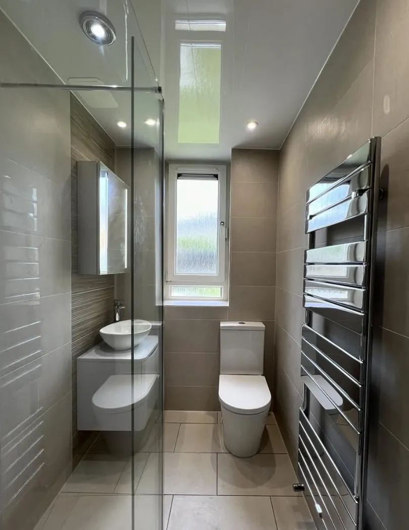 Narrow shower room with large-format grey tiling, a walk-in shower, chrome ladder radiator and a counter-top basin