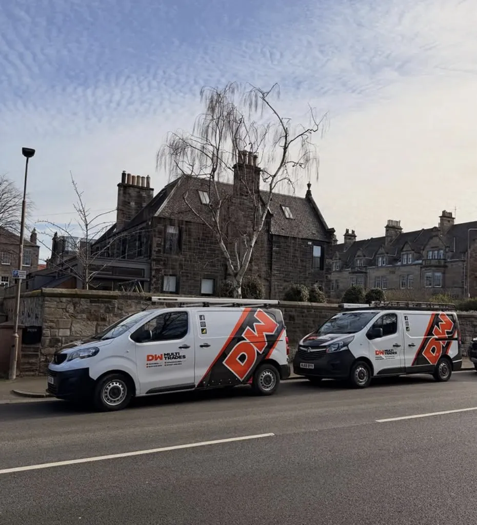 Two DW Multi Trades vans in orange and black livery parked on a street in front of traditional Edinburgh stone tenements